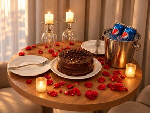 A round wooden table with a chocolate cake, two lit candles, a can of Pepsi, and scattered rose petals. - Three Pyramids Boutique Hotel (Giza)