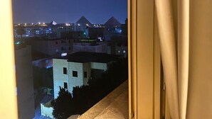 A nighttime view from a window overlooking a cityscape with pyramids in the background. - Three Pyramids Boutique Hotel (Giza)