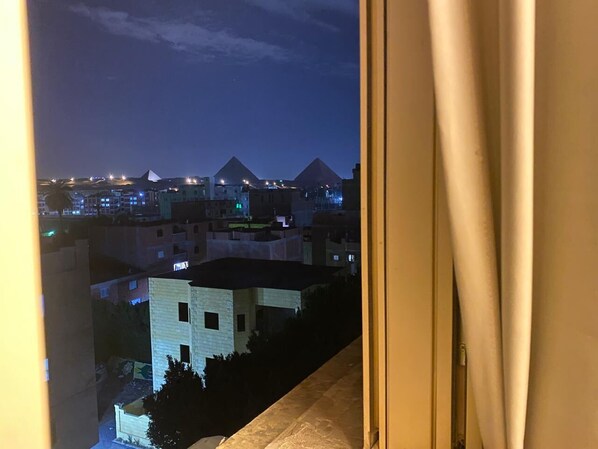 Vista nocturna desde una ventana con vistas a un paisaje urbano y pirámides al fondo.