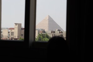 Vista de la Gran Pirámide de Giza a través de una ventana, con edificios modernos al frente.
