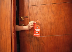 A wooden door with a brass doorknob and a hand holding a red sign with a hand symbol and the text 'PLEASE DO NOT DISTURB'. - Three Pyramids Boutique Hotel (Giza)