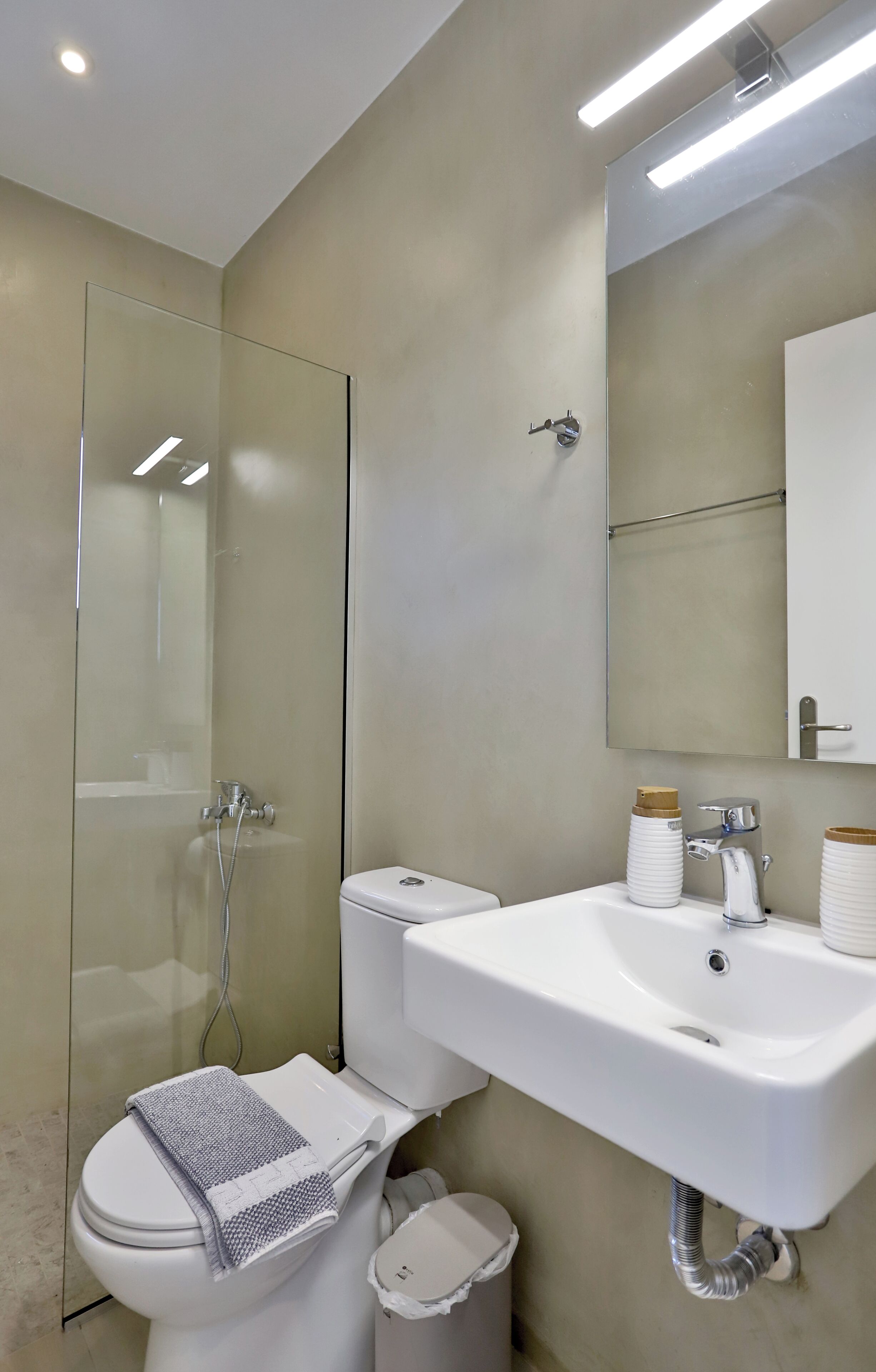 Une salle de bain moderne avec une douche à parois de verre, un lavabo blanc doté de deux compartiments et des toilettes sur lesquelles est posée une serviette.