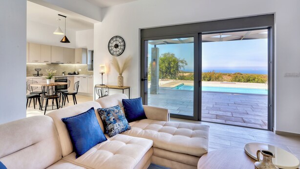 Ein modernes Wohnzimmer mit einer großen Couch, einem Essbereich und Blick auf einen Pool und die Landschaft.