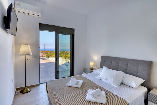 A hotel room with a bed, a floor lamp, a TV, and a sliding glass door leading to an outdoor area. - Sternes Panorama Executive Villa with Pool, Sitia (Sitia)