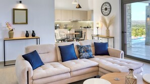 Ein modernes Wohnzimmer mit einem beigen Ecksofa, einem runden Couchtisch und einem Essbereich mit Tisch und Stühlen.