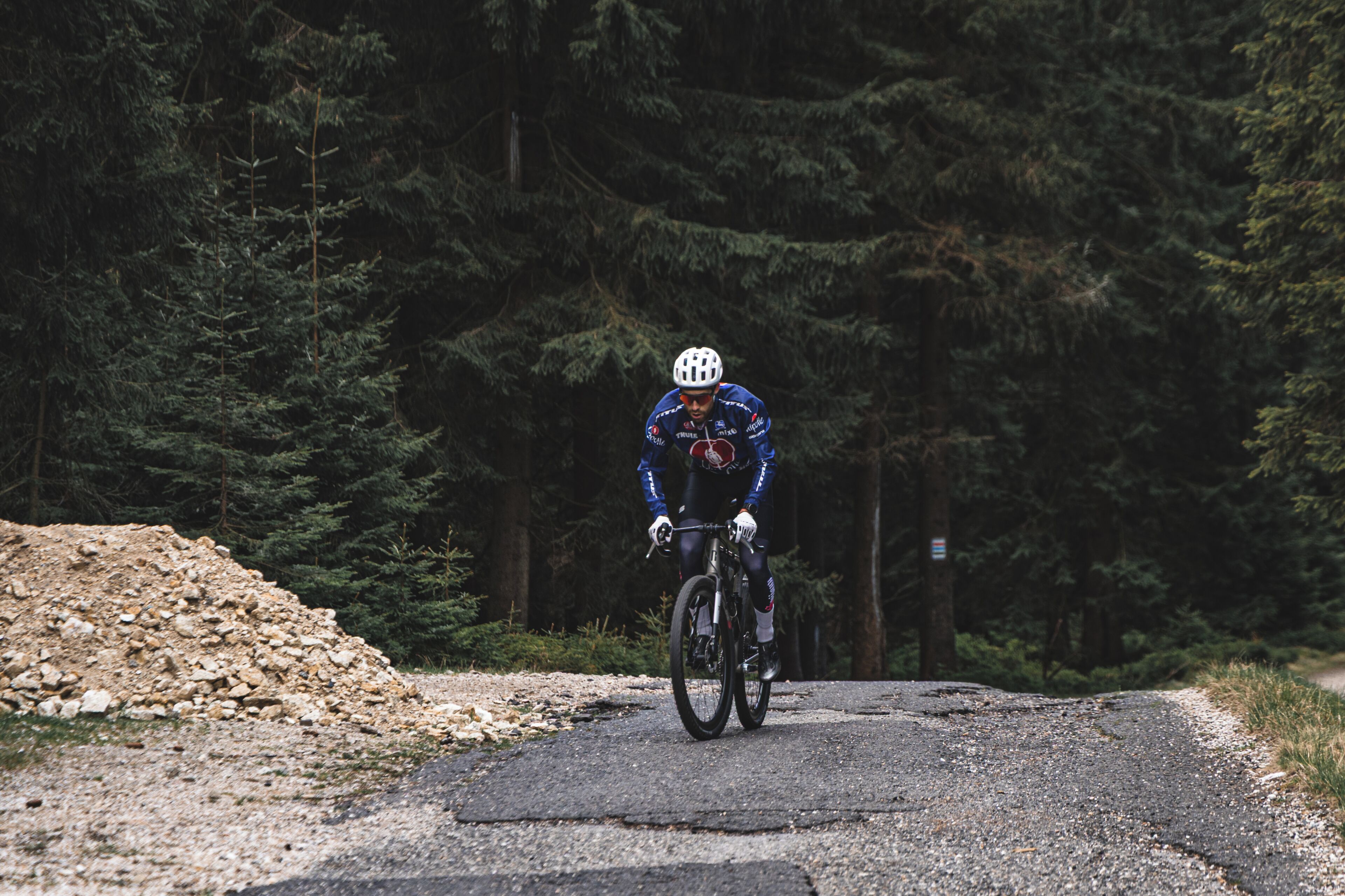 Un cycliste sur un chemin de gravier, avec une forêt dense en arrière-plan.
