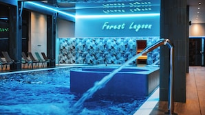A modern indoor pool area with a neon sign reading "Forest Lagoon," lounge chairs, and a water feature.