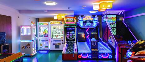Un salón recreativo con diversas máquinas de juego, incluyendo un simulador de baloncesto y un juego de carreras.