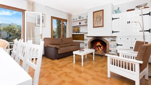 A living room with a sofa, chairs, a coffee table, a fireplace, and a view through a glass door. - Villa in Spain near Sandy Beach & Golf (Calella de Palafrugell, Llafranc)
