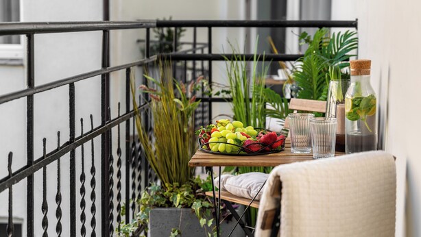 Ein Balkon mit einem Tisch, auf dem sich eine Obstschale, Gläser und eine Flasche befinden.