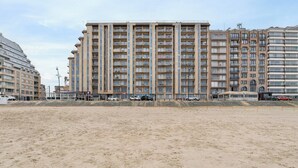 Um hotel com vários andares, fachada uniforme, varandas e uma praia arenosa em primeiro plano.