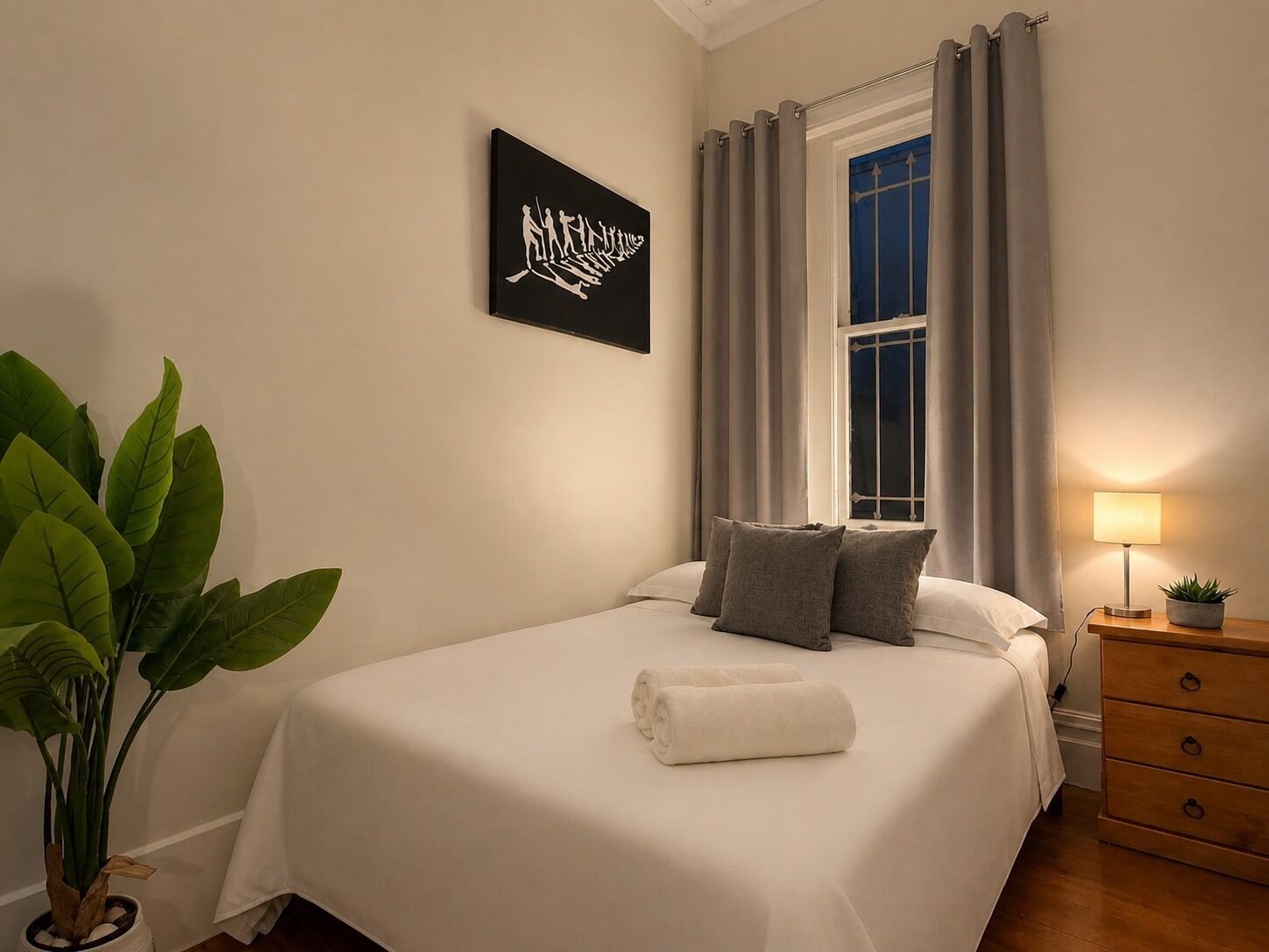 A neatly made bed with pillows, a bedside lamp, and a potted plant in a corner.