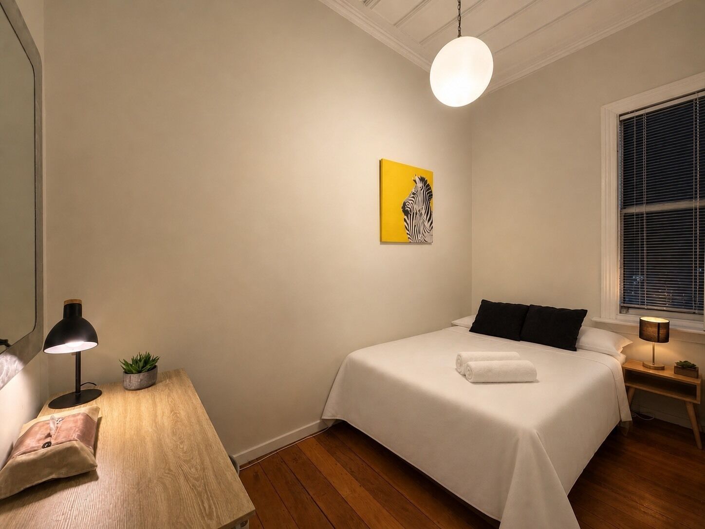 Een slaapkamer met een bed, nachtkastjes, een lamp, een potplant en een raam met jaloezieën.