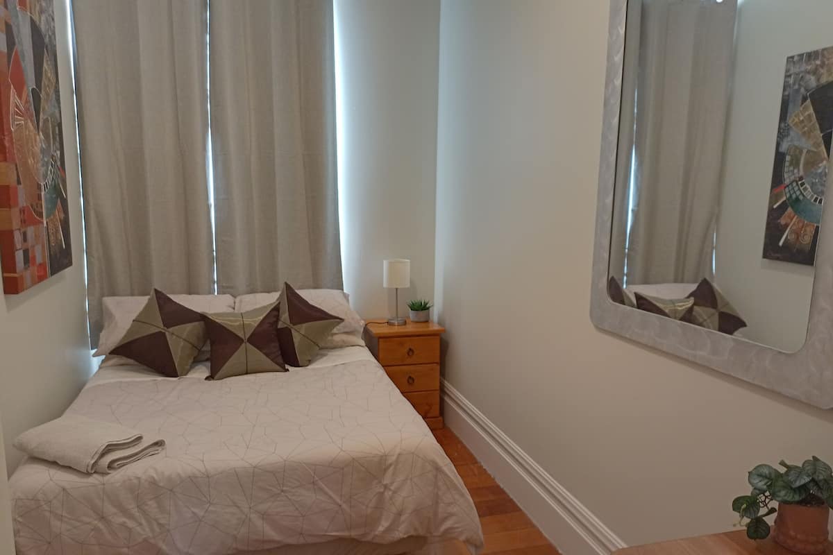 A neatly made bed with geometric patterned bedding, a bedside table with a lamp and a small plant, and a mirror on the wall.
