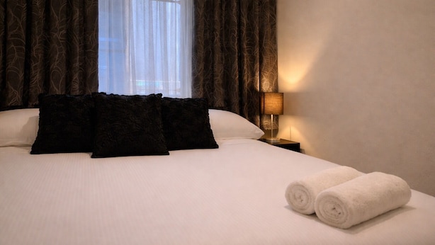 A hotel room with a bed, dark curtains, a lamp, and a window. - CitiRooms Auckland (Auckland)