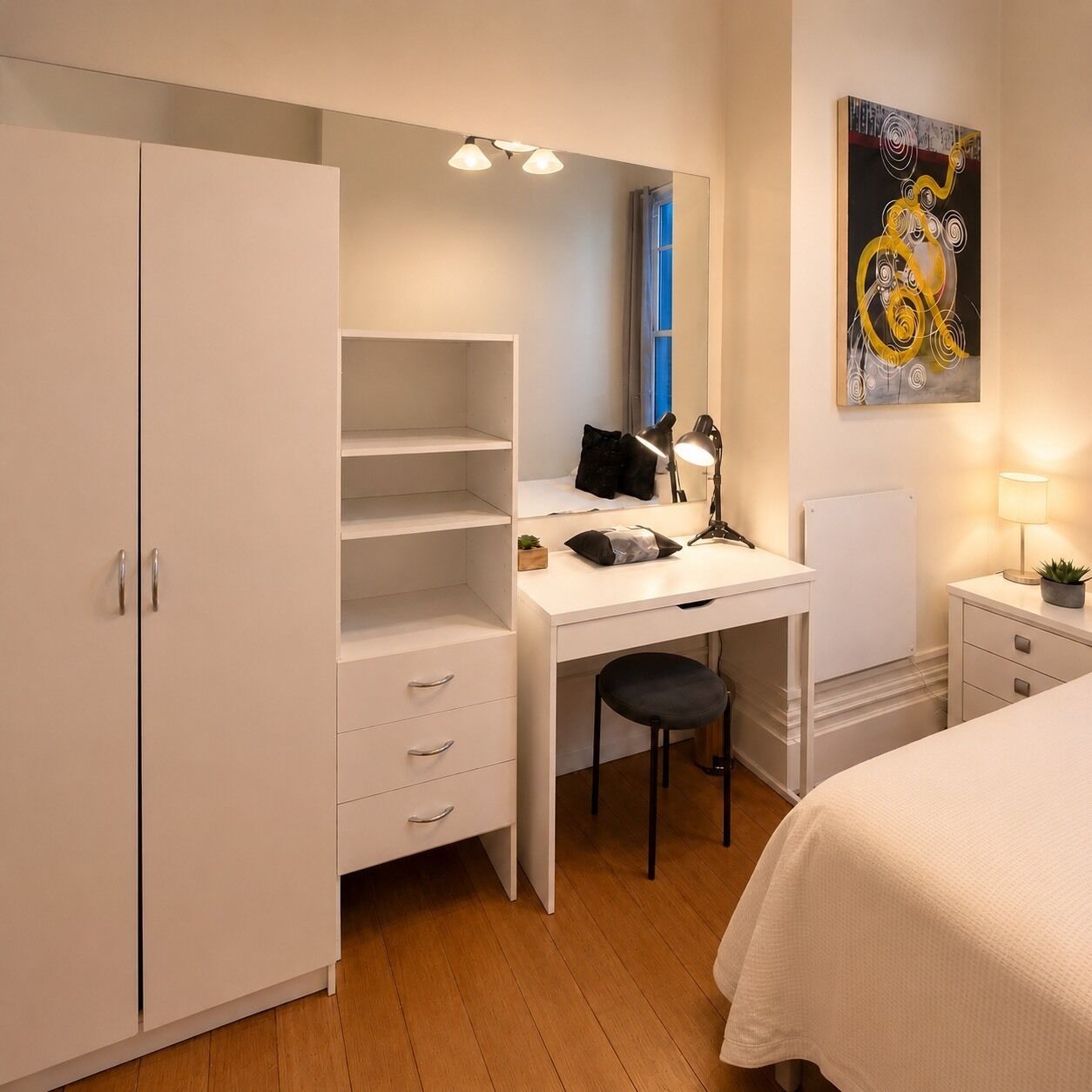 A bedroom with a bed, a desk with a chair, a wardrobe, and a painting on the wall.