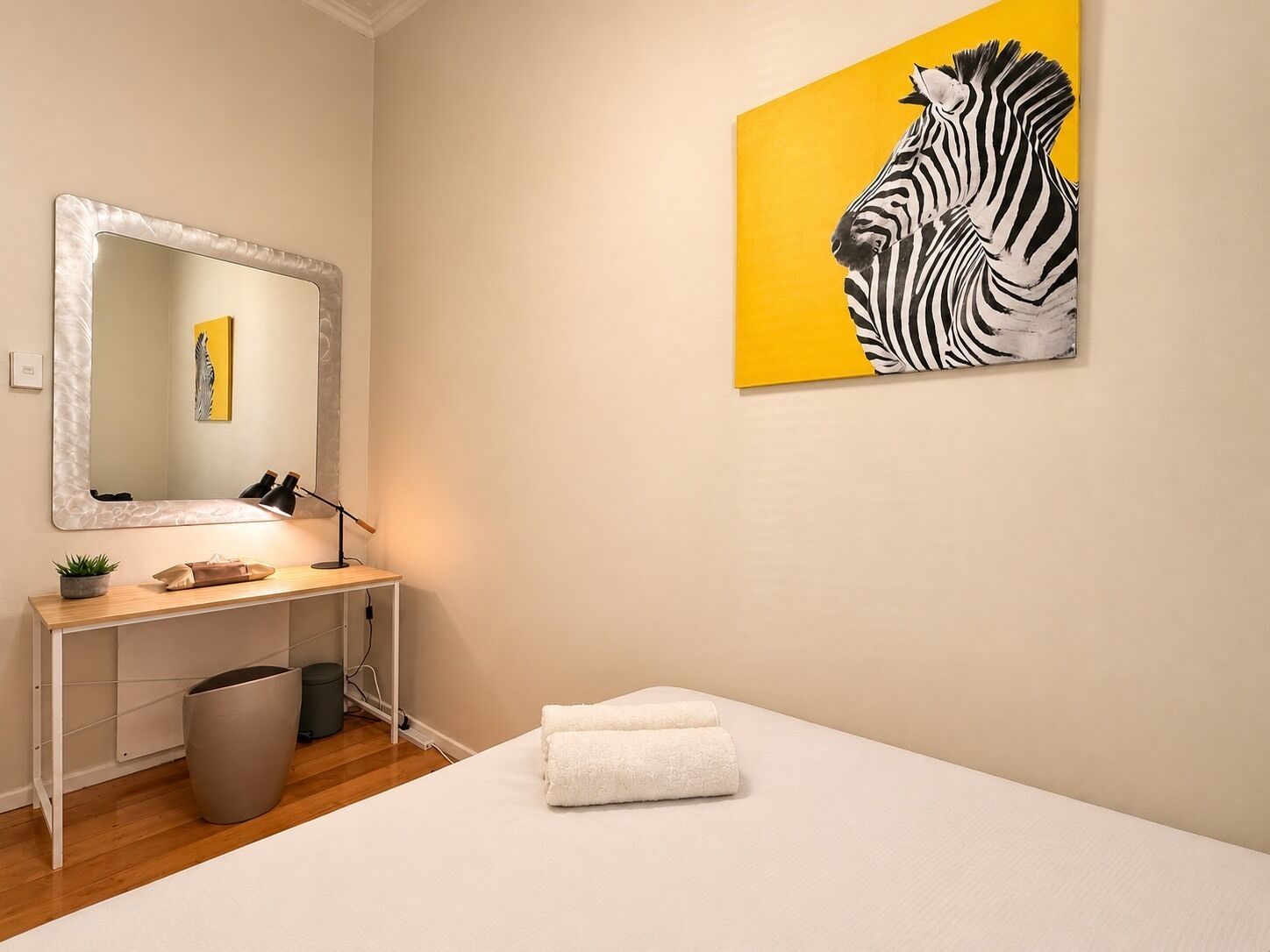 Une chambre d’hôtel avec un lit, un bureau doté d’un miroir, une poubelle et un tableau représentant une zèbre.