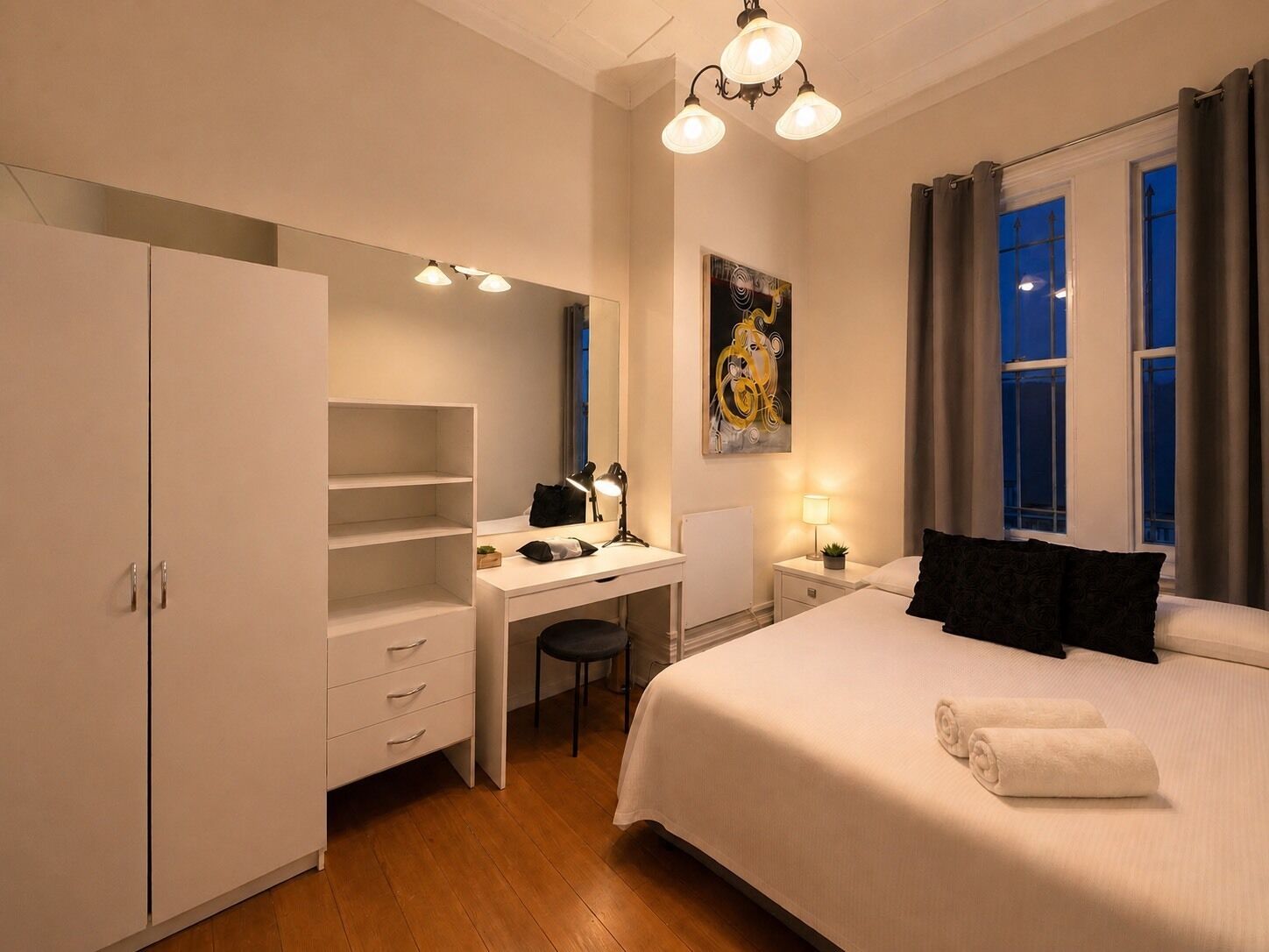 Una habitación de hotel con una cama, un escritorio, una silla, un armario y un cuadro en la pared.
