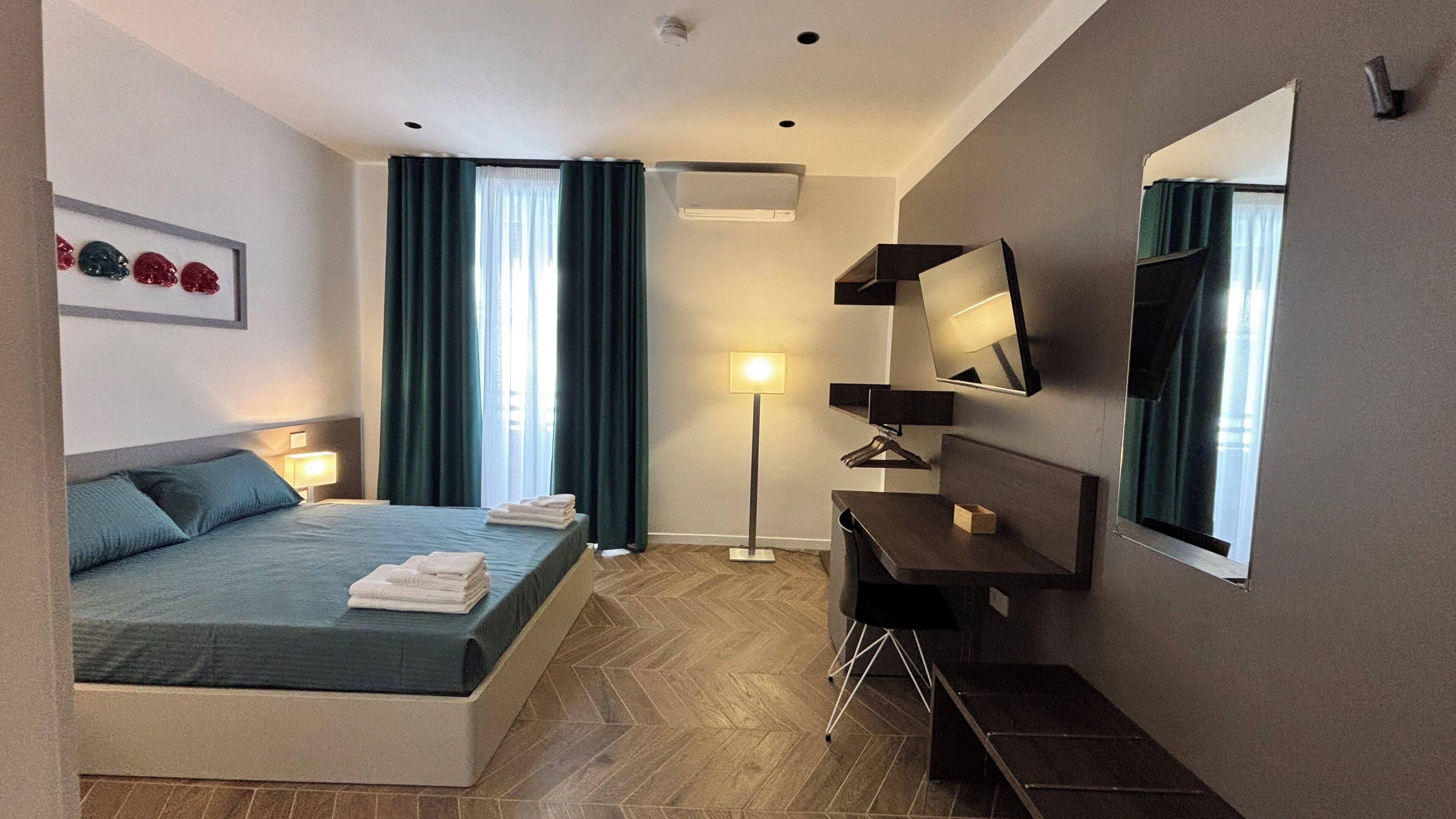A modern hotel room with a bed, a desk, a flat-screen TV, and a large window with curtains.
