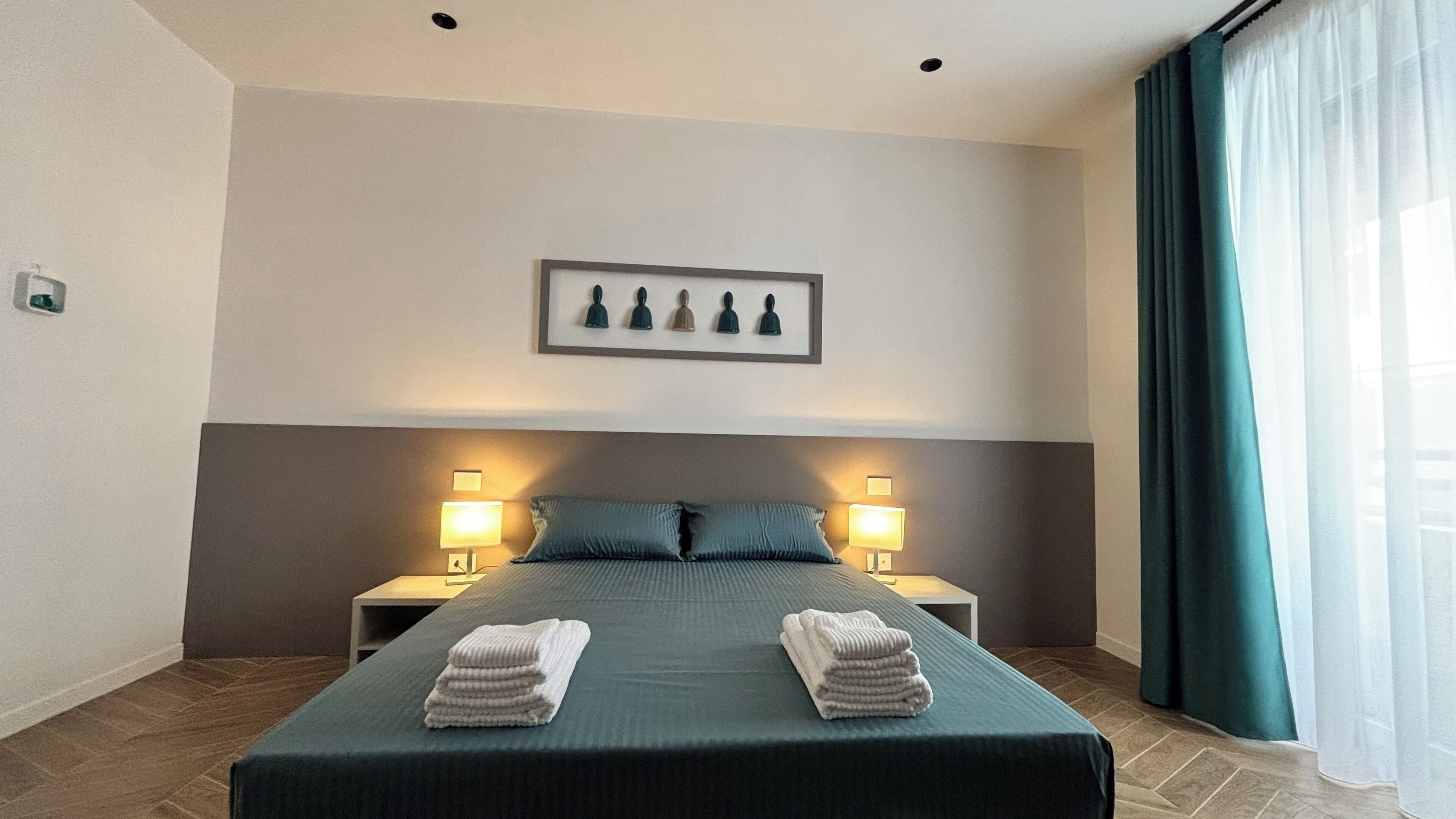 A hotel room with a large bed, two bedside tables with lamps, a framed picture on the wall, and a window with curtains.