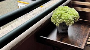 A balcony with a potted plant, a railing, and a view of a busy street with vehicles and buildings. - Seaside Suites (Naples)