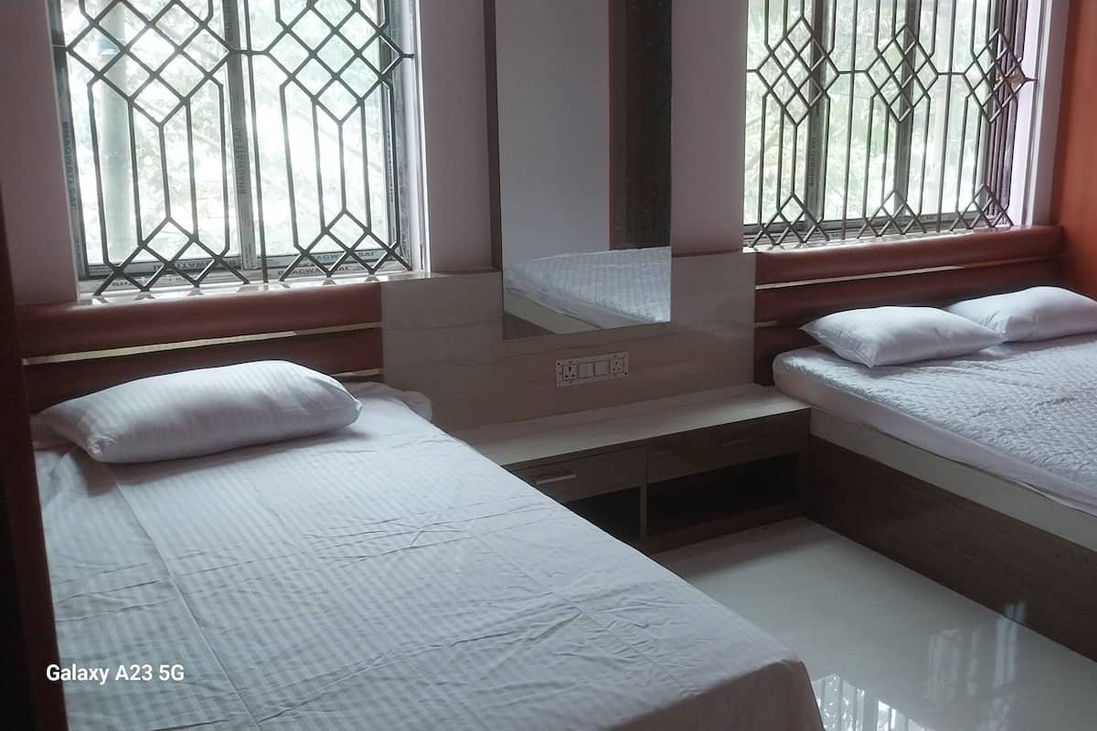 A bedroom with two single beds, a wooden nightstand, a mirror, and a window with metal bars.