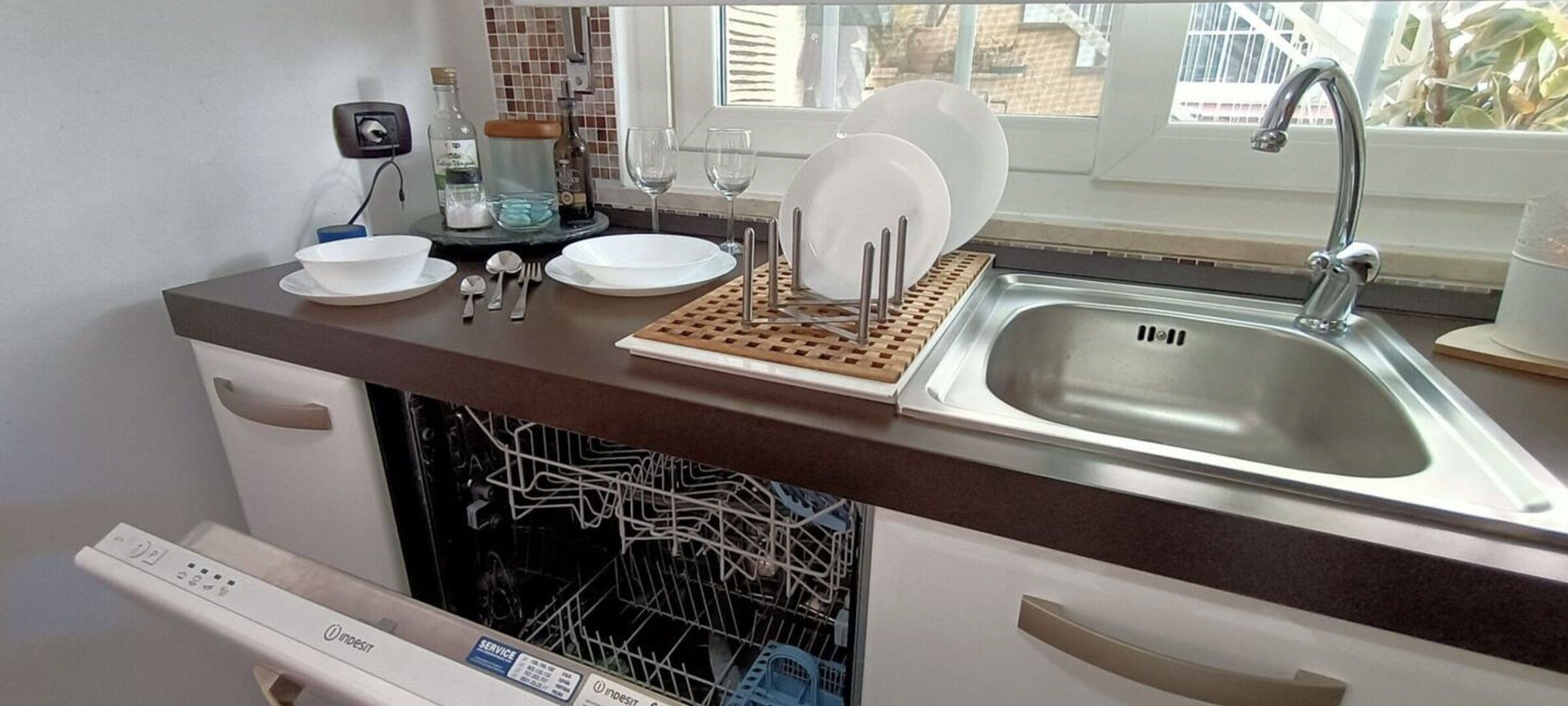A kitchen with a dishwasher, a sink, and a window with a view of buildings.
