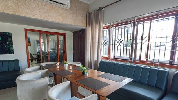 Ein modernes Wohnzimmer mit einem Holzesstisch, weißen gepolsterten Stühlen, einer Couch und einem großen Fenster mit Metallgitter.