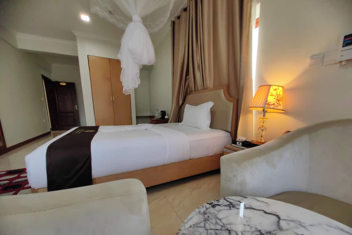 A hotel room with a bed, bedside table, lamp, and a chair.
