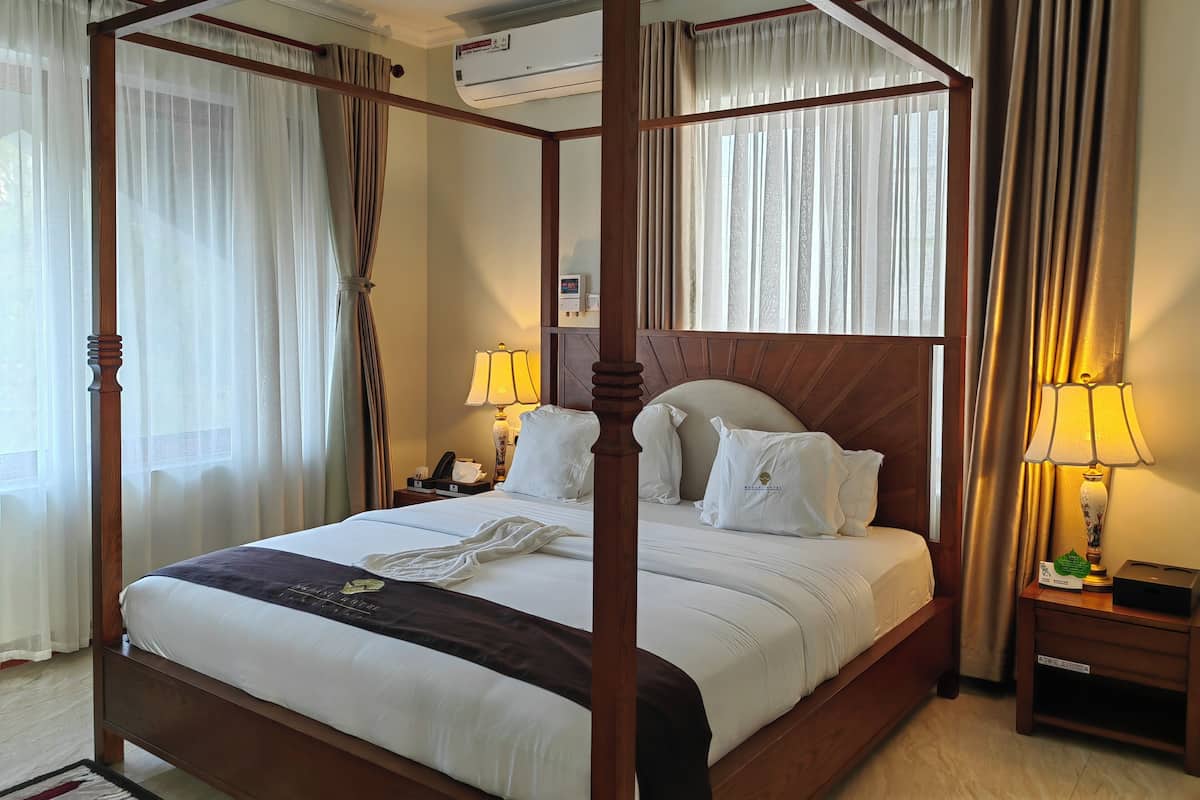 A four-poster bed with white linens, a bedside table with a lamp, and a nightstand with a phone and a box.