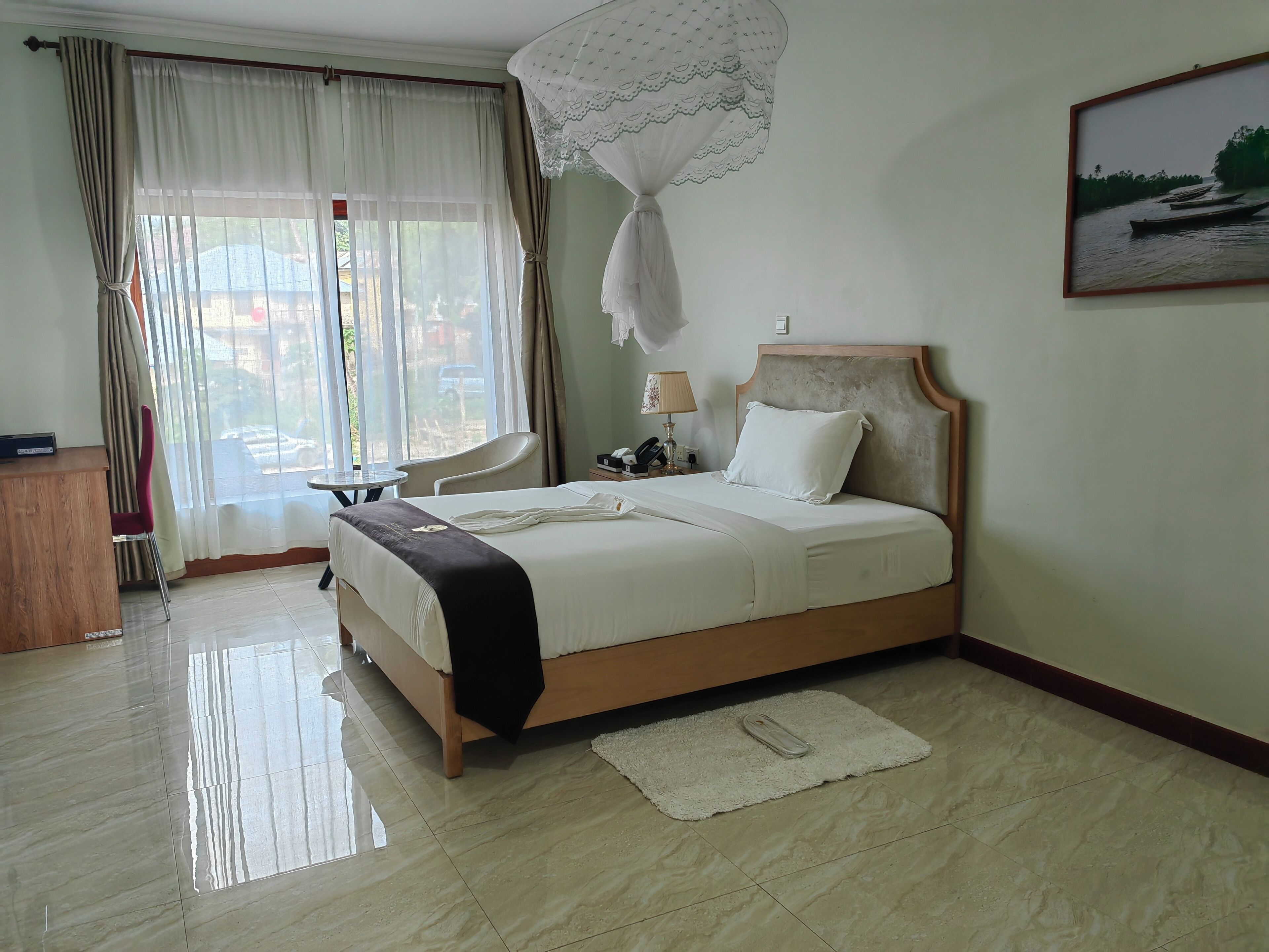Habitación de hotel con cama, escritorio, silla y ventana con cortinas.