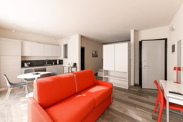 A modern apartment with a bright kitchen, a dining area, and a living room with a red sofa.