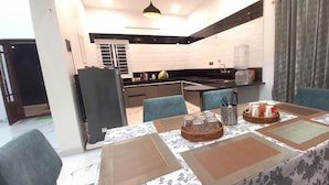 A dining area with a table set for four, a kitchen in the background, and a large water dispenser on the counter. - Orion Blu Yercuad (Yercaud)