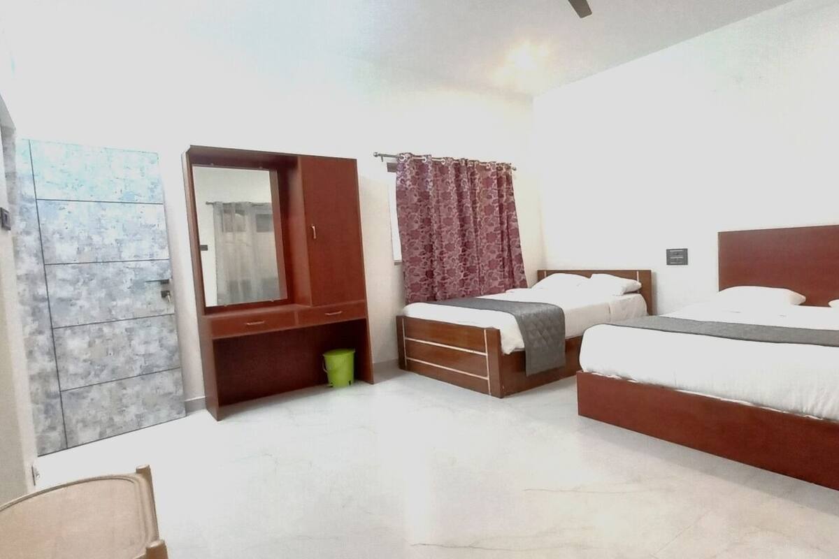A bedroom with two beds, a wardrobe, a mirror, and a window with curtains.