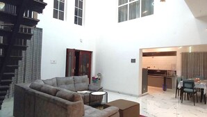 A spacious living area with a sofa, a coffee table, and a dining table set for four. A kitchen is visible in the background. - Orion Blu Yercuad (Yercaud)