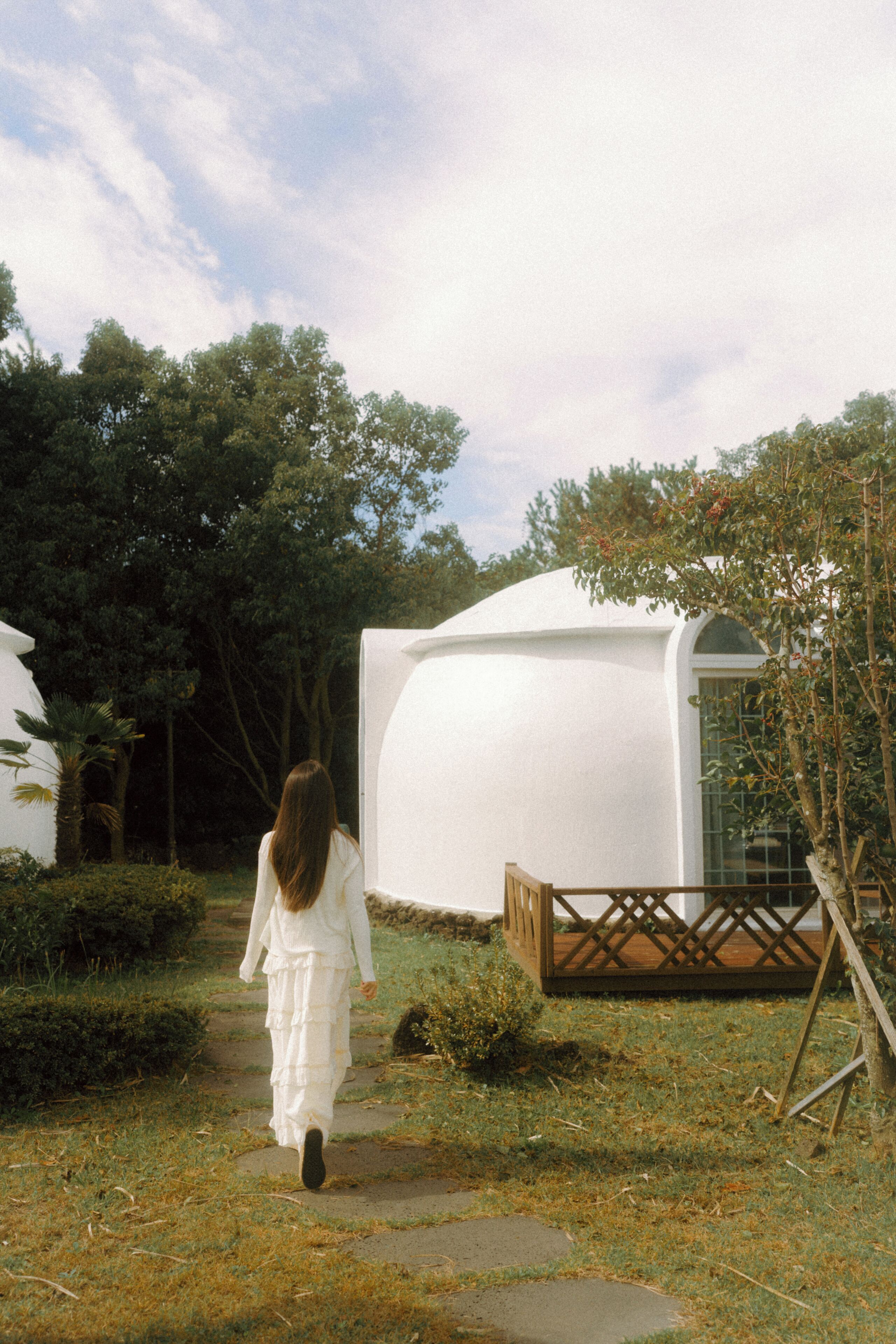 A pathway leading to a white, dome-shaped building with a wooden deck in front.