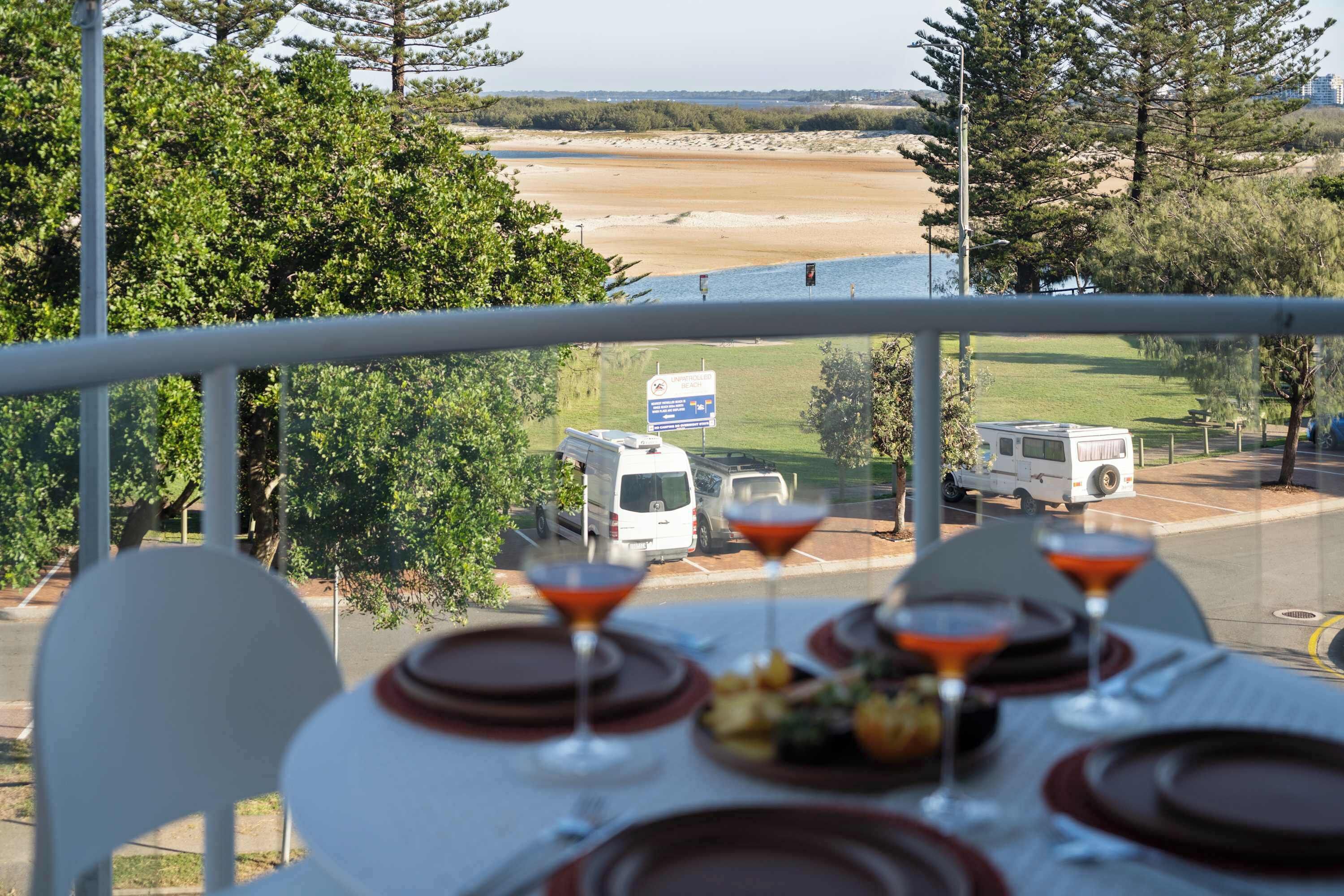 A table set for dining with a view of a beach and vehicles in the background.