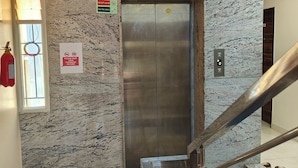 An elevator with a marble wall, a fire extinguisher, and a trash bin. - Hotel Golden Arch  (Bangalore)