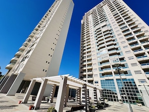 A high-rise residential building with multiple balconies, a covered outdoor area with seating, and a modern architectural design.