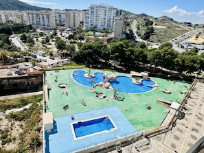A large outdoor swimming pool with multiple sections and a separate rectangular pool, surrounded by lounge chairs and sunbeds.