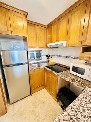 A kitchen with wooden cabinets, a stainless steel refrigerator, a microwave, and a stove.