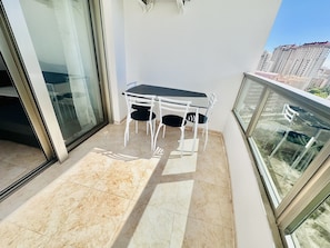 A balcony with a table and chairs, a glass door, and a view of high-rise buildings.