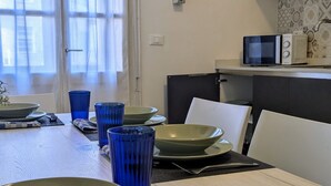 Un comedor con una mesa dispuesta para cuatro personas, incluyendo platos, tazones y vasos azules. Se ve un microondas en la encimera.