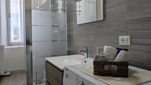 Un baño moderno con un lavabo blanco, una cabina de ducha con mampara de vidrio y un espejo sobre el lavabo.
