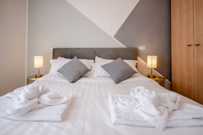 A neatly made bed with white linens and gray pillows, two bedside lamps, and a wooden wardrobe. - VivimiHome - Zanella House (Milano)