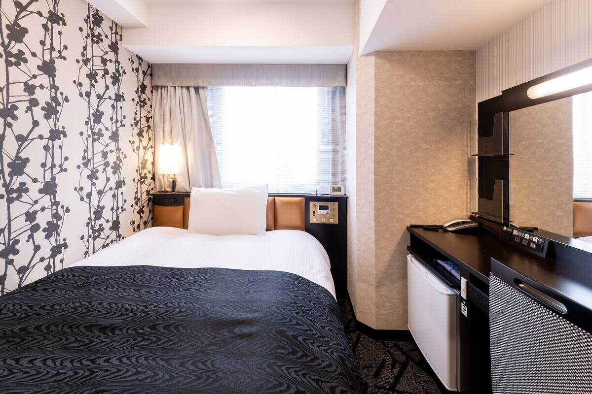 Une chambre d’hôtel avec un lit, un bureau, une chaise, une télévision et une fenêtre avec des rideaux.