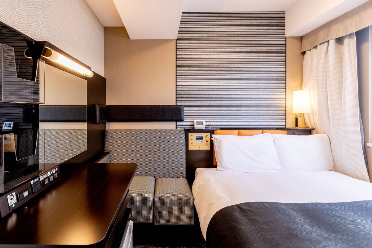 Une chambre d’hôtel comprenant un lit, un bureau, une chaise, une table de chevet avec une lampe et un grand miroir.