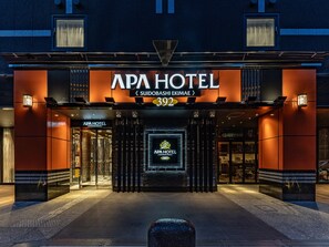 Exterior del hotel APA, con una fachada moderna, portones de entrada y señalización iluminada.