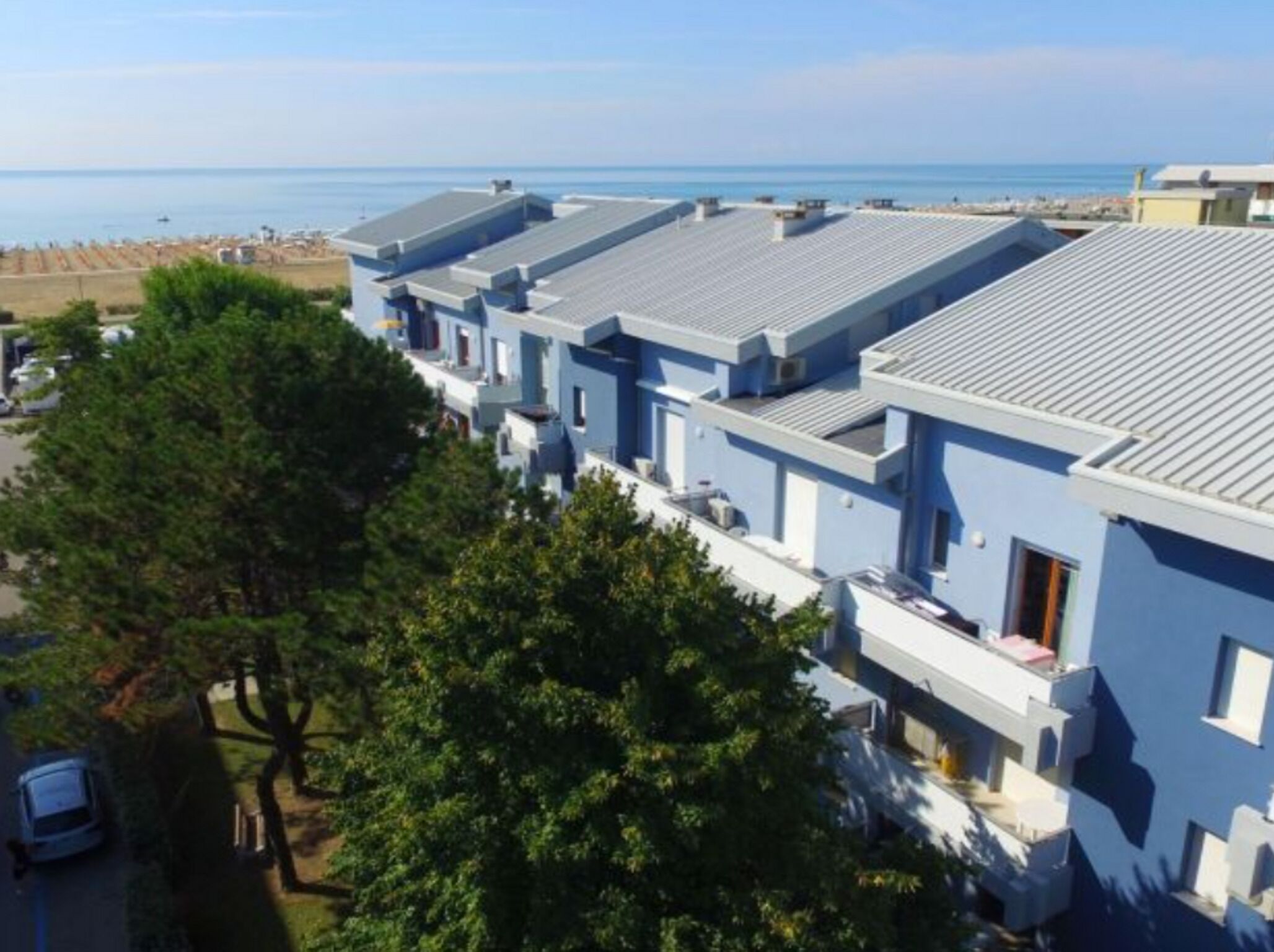 En rad moderna, ljusblå byggnader med platta tak, troligen en del av ett hotell eller semesteranläggning, med utsikt över en strand och havet.