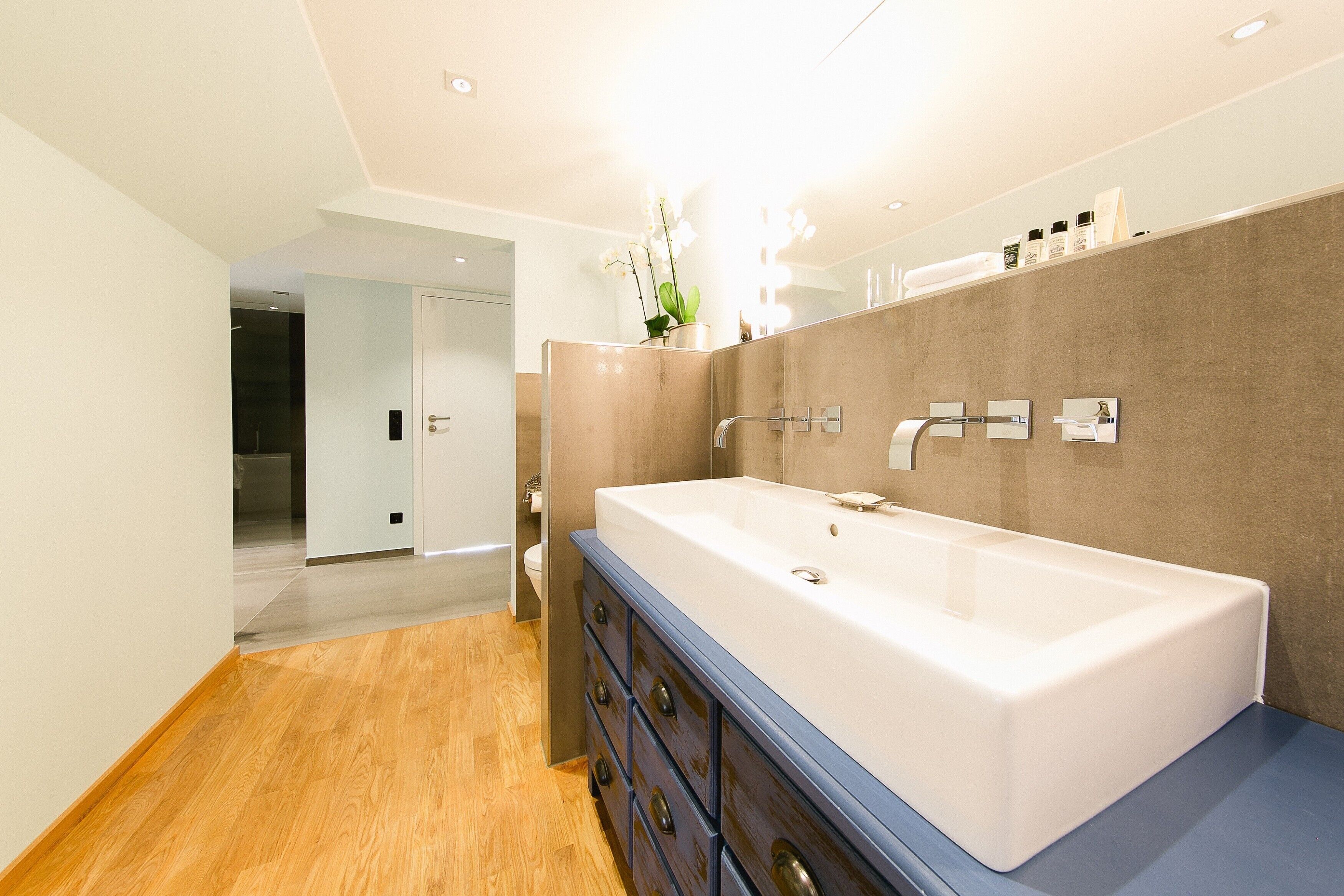 A modern bathroom with a large white bathtub, wooden floor, and a mirror with toiletries.